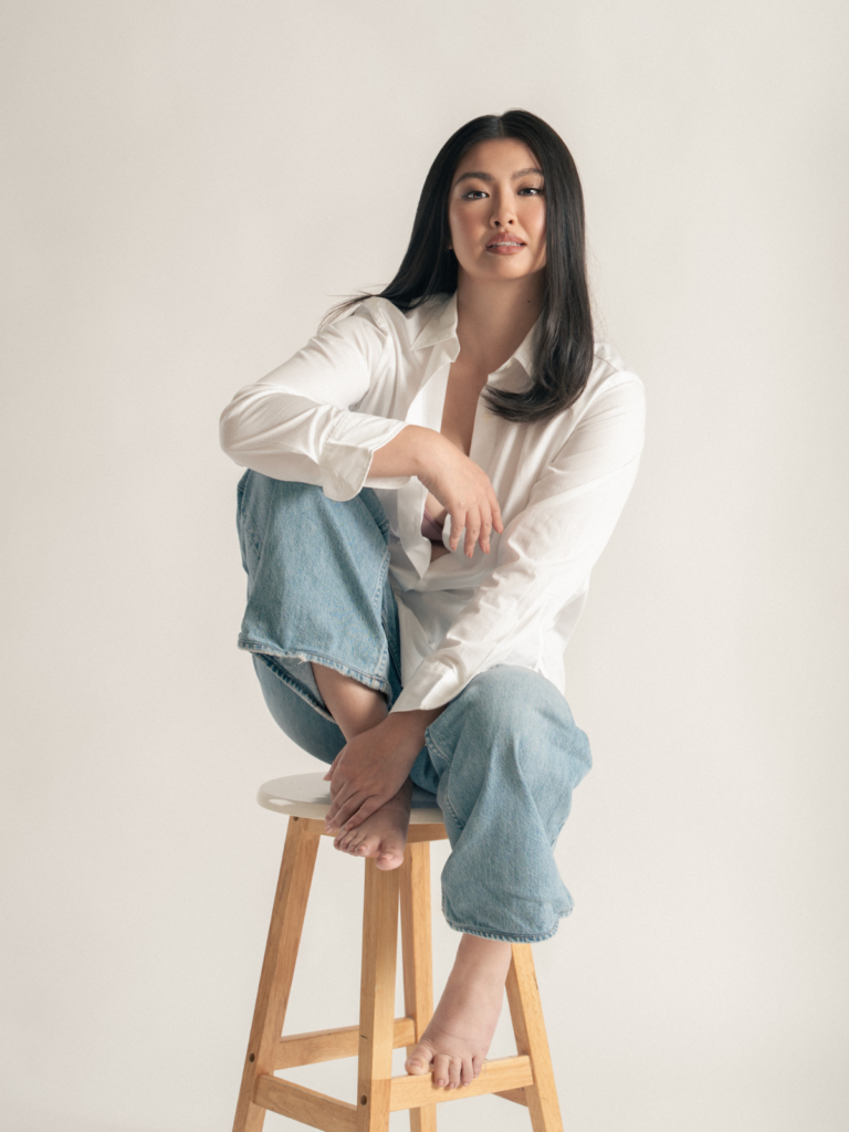 Giannina sitting on a stool wearing jeans and a white shirt